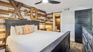 A bedroom with a wooden headboard, a bed with patterned pillows, a ceiling fan, and a dark wooden dresser. - Ground floor unit with rustic flair (Destin)
