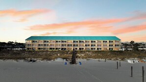 A multi-story hotel with a green roof, located near a beach with sand and wooden posts. - Ground floor unit with rustic flair (Destin)