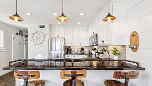 A modern kitchen with white cabinets, a central island with stools, pendant lighting, and a ship's wheel decoration. - Ground floor unit with rustic flair (Destin)