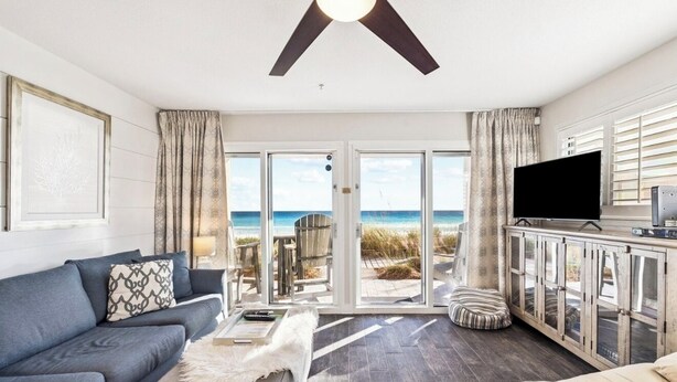 A living room with a sofa, a coffee table, and a TV. There is a large window with a view of the beach. - Ground floor unit with rustic flair (Destin)