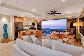 A modern living room with a sofa, dining area, kitchen, and a large window with a view. - Private Rooftop Pool - Ocean View Romantic Getaway (Cabo San Lucas)