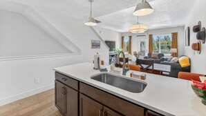 Une cuisine moderne dotée d’un grand îlot central, un coin repas avec une table et des chaises, et un salon avec un canapé et un téléviseur.