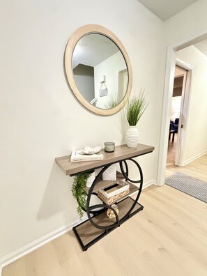Een hal met een ronde spiegel, een console tafel met decoratieve objecten, en een deur naar een andere kamer.