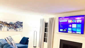 Ein modernes Wohnzimmer mit einem großen, blauen Sofa, einem Holztisch und einem Flachbildfernseher über einem Kamin.