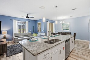 A modern kitchen with a central island, built-in appliances, and a dining area with a gray sofa and a small table. - Orlando Getaway w/ Private Pool & Lazy River (Davenport)