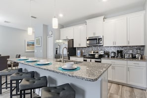 A modern kitchen with white cabinets, granite countertops, a central island with bar stools, stainless steel appliances, and pendant lighting. - Orlando Getaway w/ Private Pool & Lazy River (Davenport)