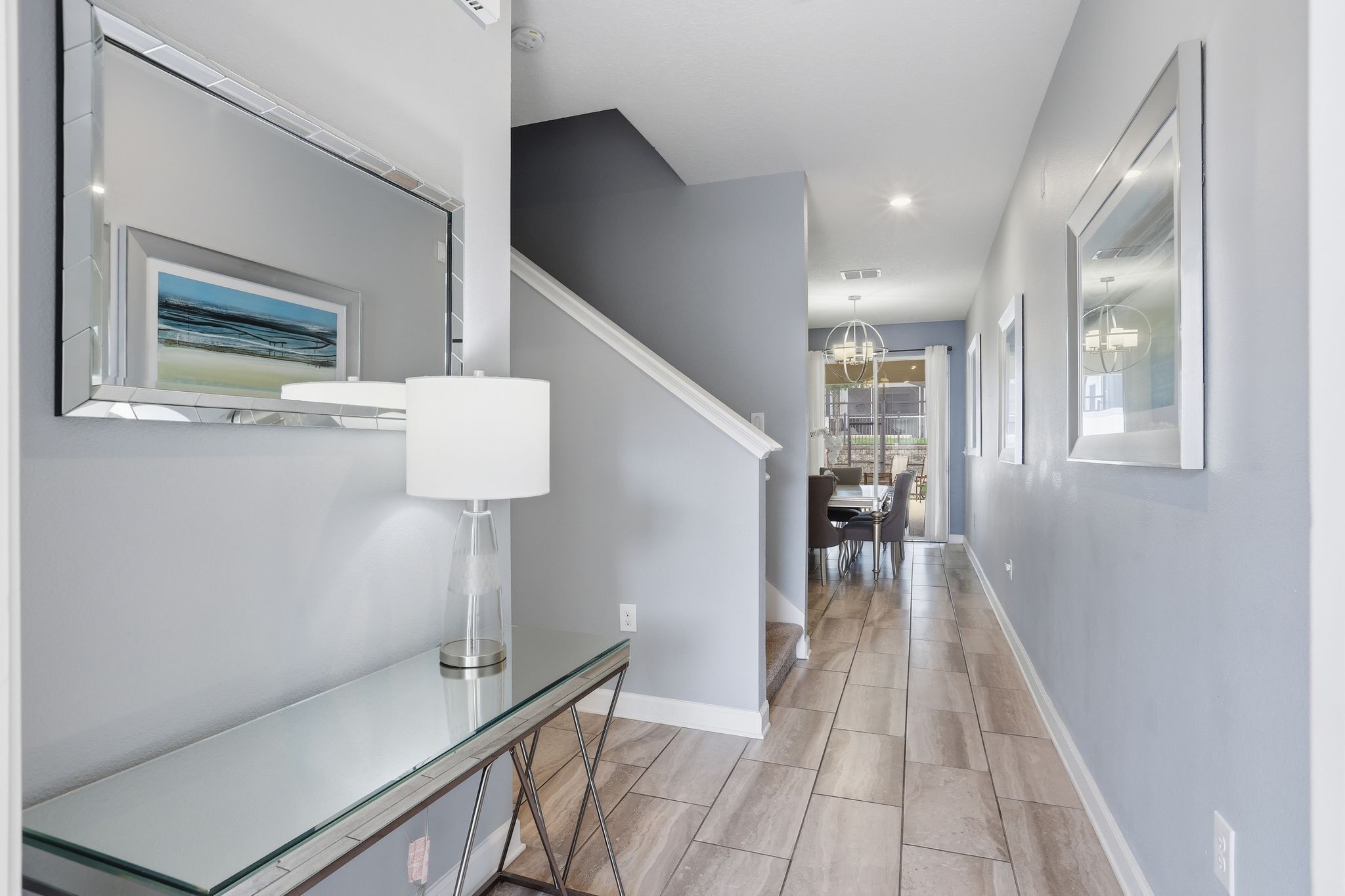 A modern hallway with a glass console table, a staircase, and a dining area in the background.