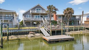 A waterfront property with a multi-level house, a wooden dock, and a clear view of the water. - Sunsets, Sand & Boat-Ready Getaway (Holden Beach)