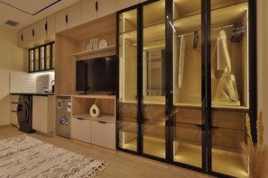 A modern kitchen with a built-in oven, refrigerator, and a microwave. There is a wooden cabinet with a television above it. - Luxury Studio with Bathtub Steps to City Stars (Cairo Governorate)