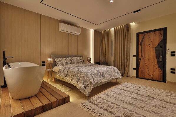 Un dormitorio moderno con una cama grande, una bañera y piso de madera.