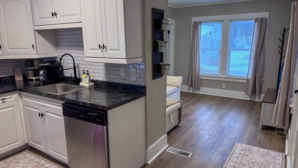 A modern kitchen with white cabinets, a black countertop, and a dishwasher. There is a window with blinds and a rug on the floor. - Serene 1-bedroom house in welcoming Slippery Rock (Slippery Rock)