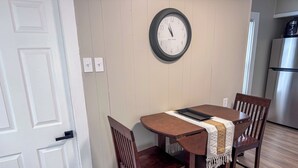 A dining area with a wooden table, two chairs, a clock, and a refrigerator in the background. - Serene 1-bedroom house in welcoming Slippery Rock (Slippery Rock)