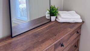 A wooden dresser with a mirror, a potted plant, and folded towels. - Serene 1-bedroom house in welcoming Slippery Rock (Slippery Rock)