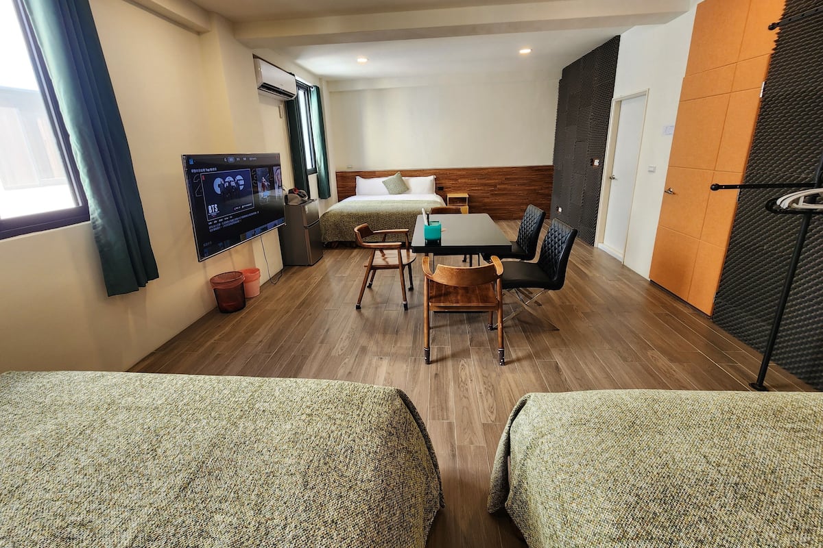 A hotel room with a bed, a TV, a desk with chairs, and a window with curtains.