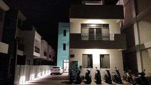 Ein modernes Gebäude mit befestigtem Eingang, ein weißes Auto vor der Fassade und mehrere Roller vor dem Haus.
