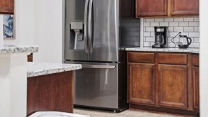 Un refrigerador de acero inoxidable con dispensador de agua, armarios de madera, salpicadero de azulejos y una cafetera sobre la encimera.
