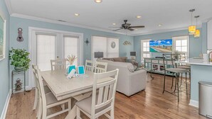 A spacious living area with a dining table, seating, a ceiling fan, and a kitchen area with a view of the beach. - Charleston Village 201 (North Myrtle Beach)