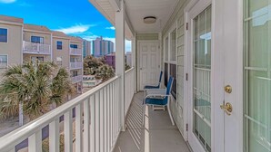 A balcony with a white railing, a door, and a chair. - Charleston Village 201 (North Myrtle Beach)