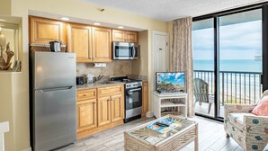 A compact kitchen with modern appliances, a dining area with a glass table, and a balcony with a view. - Beach Colony 603 (Myrtle Beach)