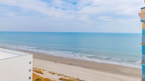 A beach view with a building on the left, a clear sky, and calm sea. - Ocean Escape 1227 (Myrtle Beach)
