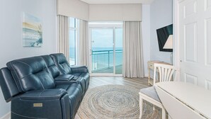 A modern living room with a reclining sofa, a small table, a TV, and a view of the sea through large windows. - Ocean Escape 1227 (Myrtle Beach)