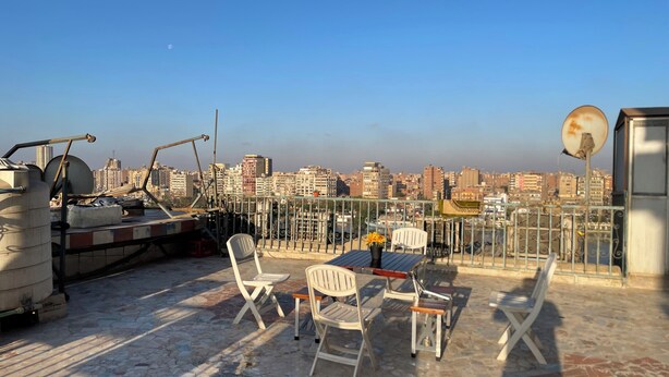 Une terrasse sur le toit offrant une vue sur le paysage urbain, avec une table et des chaises, une antenne parabolique et du matériel de construction.