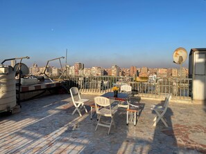 Une terrasse sur le toit offrant une vue sur le paysage urbain, avec une table et des chaises, une antenne parabolique et du matériel de construction.