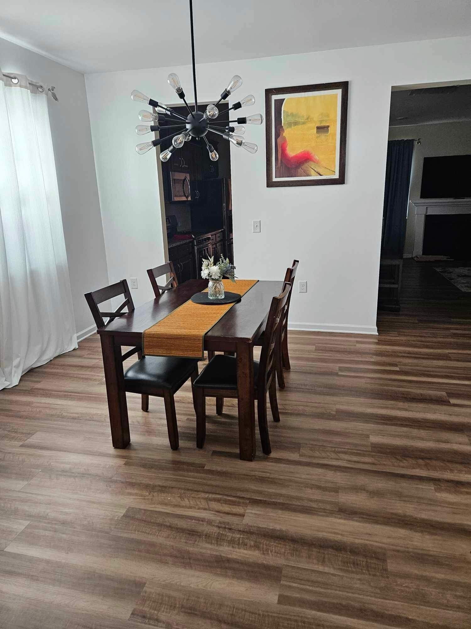 Un coin repas avec une table en bois, des chaises, un vase de fleurs, un luminaire moderne et un tableau encadré accroché au mur.