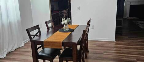 Un coin repas avec une table en bois, des chaises, un vase de fleurs, un luminaire moderne et un tableau encadré accroché au mur.