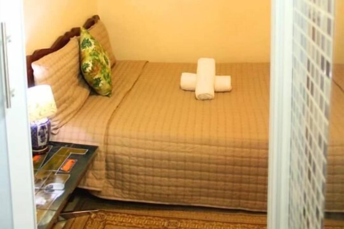 A small, cozy room with a single bed, a bedside table with a lamp, and a unique ceiling light fixture.