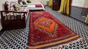 A room with a patterned floor, a bed with a red and orange rug, a wooden bench, and a hanging light fixture. - Riad Dar Babouche (Fes)