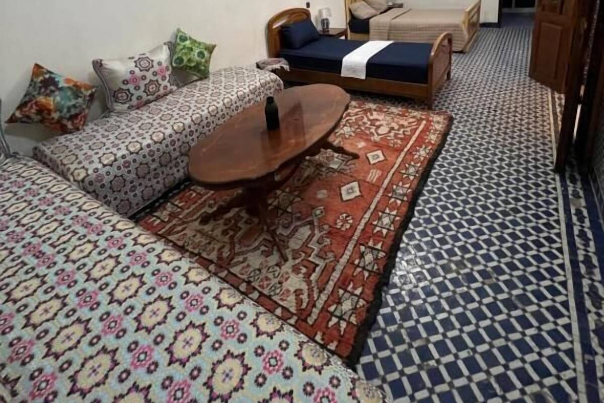 A small, cozy room with a sofa, a bed, a wooden table, and patterned rugs.