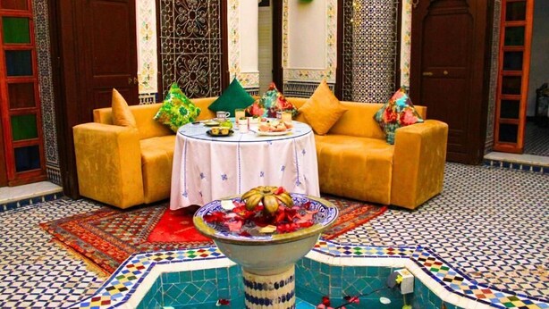 A Moroccan-style interior with a sofa set, a table with food, and a decorative fountain. - Riad Dar Babouche (Fes)