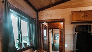 Un intérieur en bois avec une table ronde et des chaises, un réfrigérateur et une fenêtre avec des rideaux.