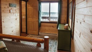 Une chambre dans un chalet en bois, avec un lit, un bureau, une fenêtre avec des rideaux et une vue sur une forêt.