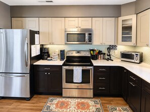 A modern kitchen with stainless steel appliances, dark cabinetry, and a patterned rug.