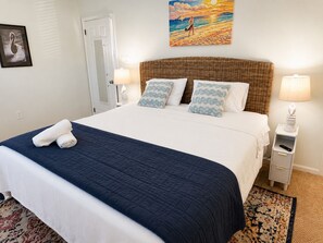 A hotel room with a bed, two pillows, a nightstand, a lamp, a painting, and a door.