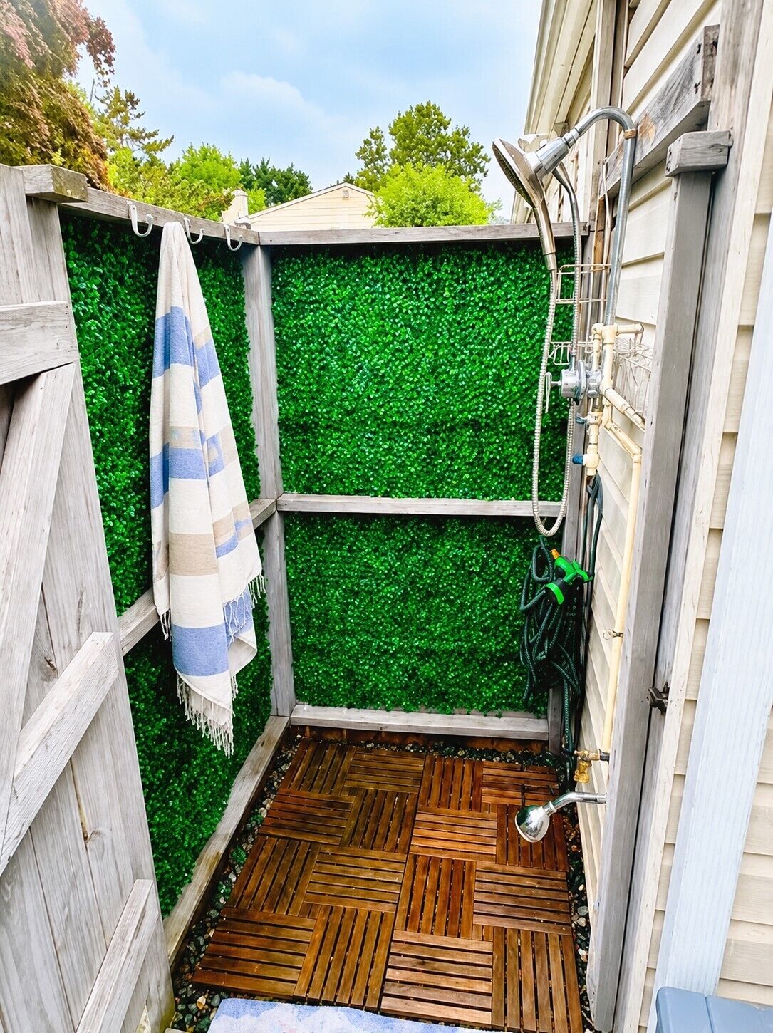 Eine Holzterrasse mit einer Wand aus grünem Kunstgrün, Holzboden und einem Duschbereich mit Brause.