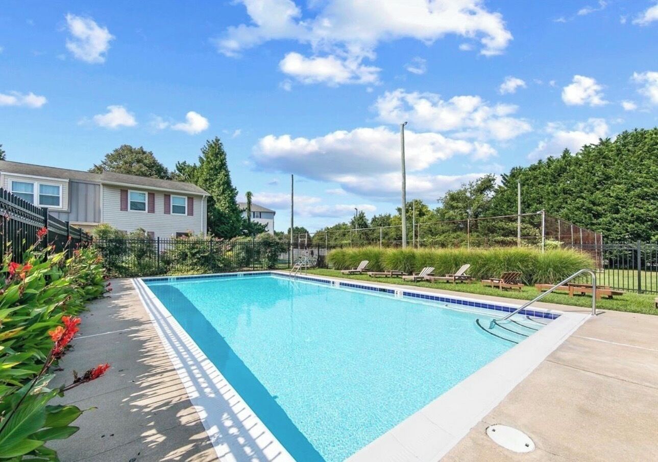 Une piscine rectangulaire aux parois bleues, entourée d’une terrasse en béton. On aperçoit des chaises longues et une clôture à l’arrière-plan.