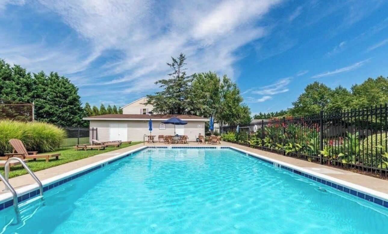 Ein Swimmingpool mit Liegestühlen, einer überdachten Sitzgelegenheit und einem eingezäunten Garten.