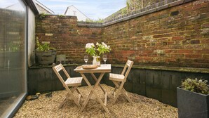 A small outdoor patio with a table and two chairs, surrounded by a brick wall and a window. - An Selder - Near waterfront, pet allowed, Wifi (Fowey)