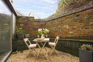 A small outdoor patio with a table and two chairs, surrounded by a brick wall and a window. - An Selder - Near waterfront, pet allowed, Wifi (Fowey)