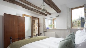 A bedroom with a bed, wooden wardrobe, stone wall, window with flowers, and exposed wooden beams. - An Selder - Near waterfront, pet allowed, Wifi (Fowey)