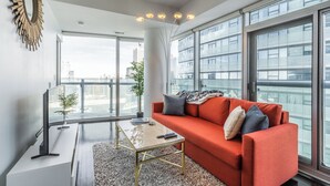 Uma sala de estar moderna com um sofá vermelho, uma mesa de centro de vidro e vista para um horizonte urbano através de grandes janelas.
