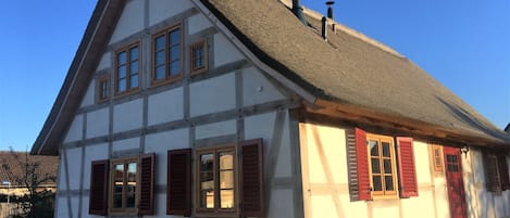 A traditional half-timbered house with a steeply pitched roof, multiple windows with shutters, and a chimney.
