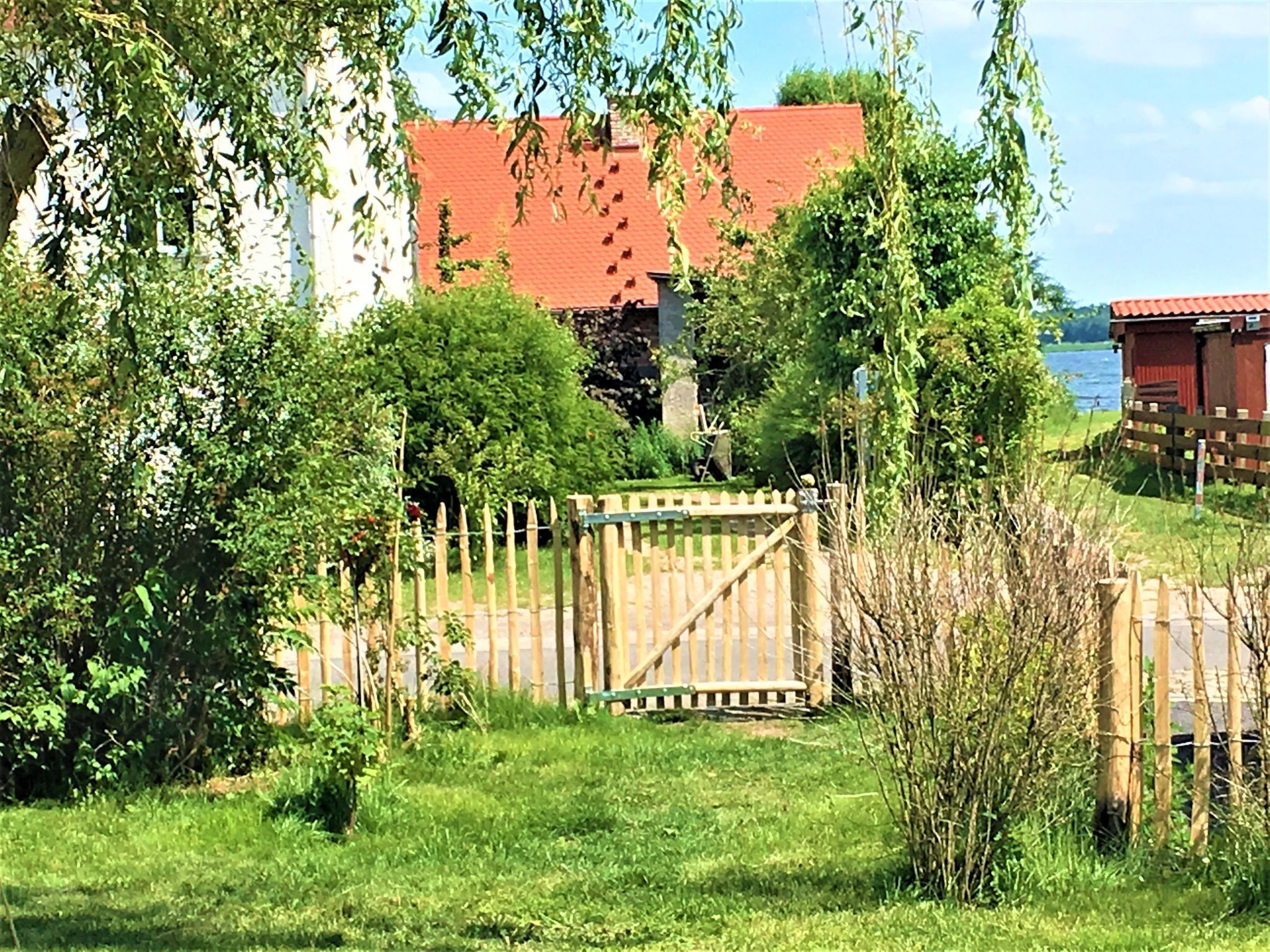 Ein ländliches Anwesen mit einem Holztor, üppiger Vegetation und einem Gebäude mit rotem Dach.