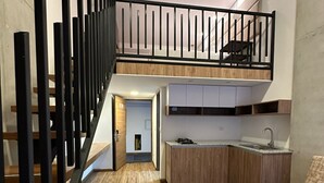 Um apartamento moderno com piso de madeira, uma escada com corrimão preto, área de cozinha com armários brancos e um sofá.