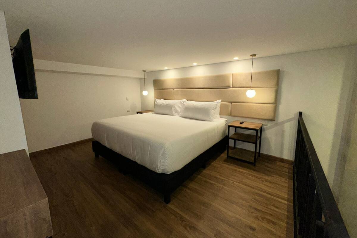 A bedroom with a large bed, a nightstand, and a wall-mounted TV.