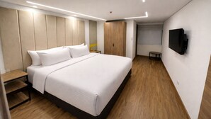 Quarto de hotel moderno com uma cama grande, uma mesa de cabeceira de madeira, uma pequena mesa e uma TV de tela plana na parede.