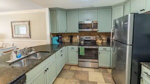 A kitchen with light green cabinets, a stainless steel refrigerator, a microwave, an oven, and a granite countertop. - Spacious 3-bedroom condo in the heart of Tybee Island. Easy beach access. (Tybee Island)